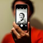 Person taking a selfie with a smartphone, illustrating privacy questions around uploading personal photos to AI services