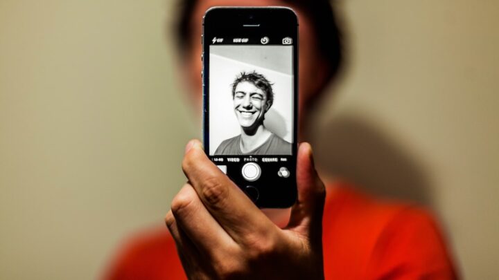 Person taking a selfie with a smartphone, illustrating privacy questions around uploading personal photos to AI services
